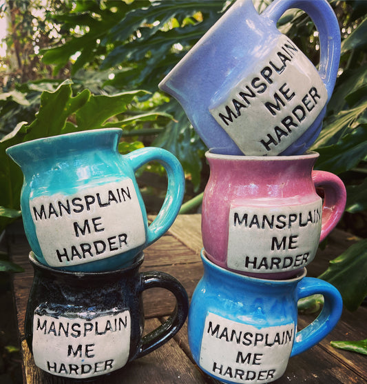  A ceramic coffee mug featuring the phrase ‘Mansplain Me Harder’ in bold text, challenging gender stereotypes and advocating for equality