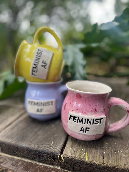A ceramic coffee mug with ‘Feminist AF’ boldly printed in empowering text, celebrating gender equality and women’s rights